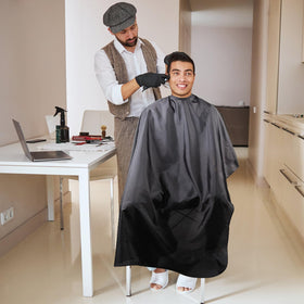 Cape de coupe de cheveux Omvoina noire avec un coiffeur en action