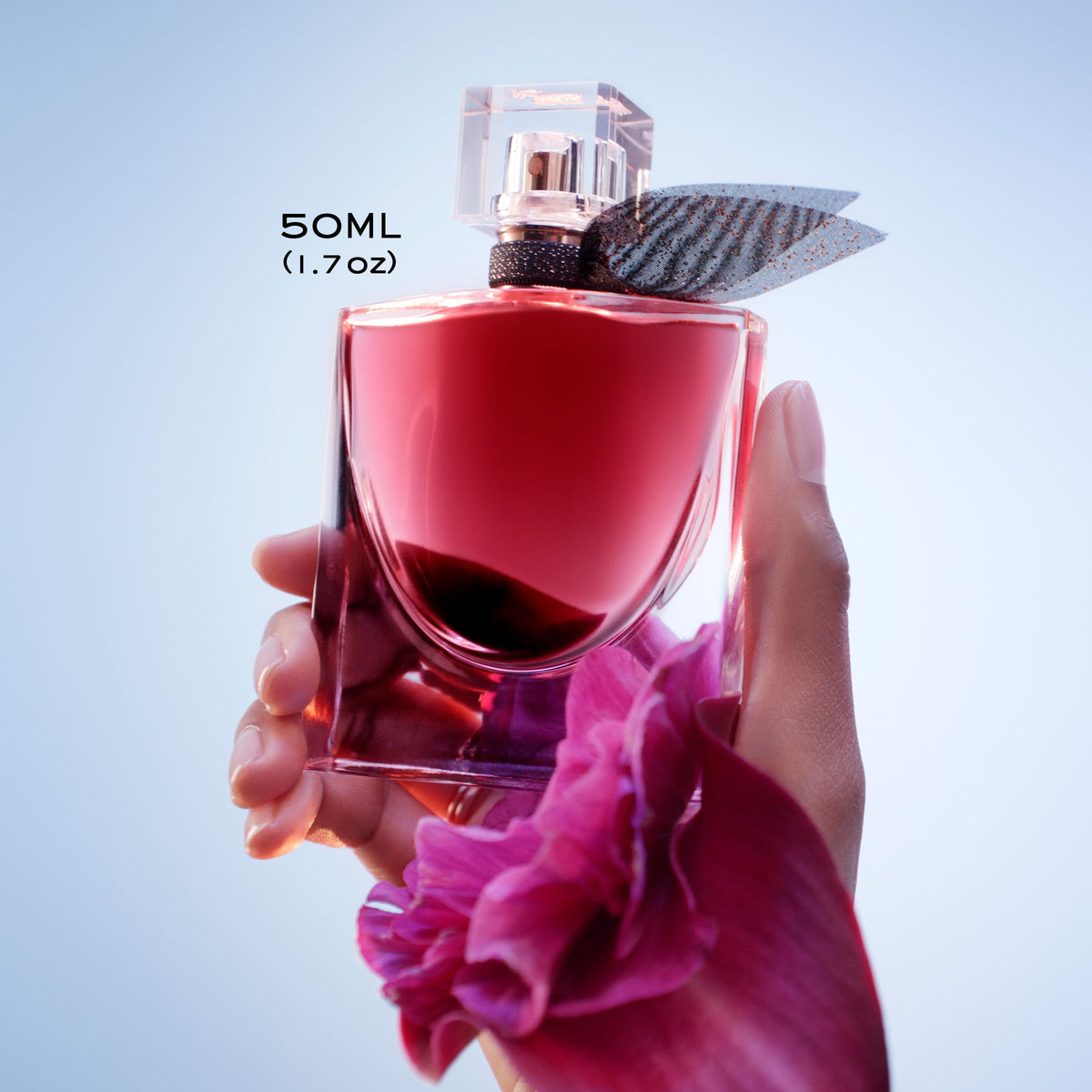 Flacon de parfum L'Elixir avec des fleurs en arrière-plan