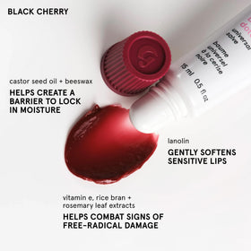Glossier Balm Dotcom tube sur une table avec des fleurs en arrière-plan