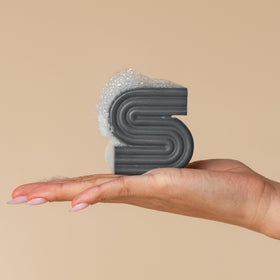 Kitsch Shampoo Bar Clarifiant 100g à côté de bouteilles de shampooing liquide