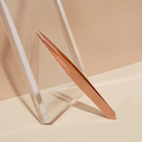 Pince à épiler Tweezerman sur un fond de maquillage